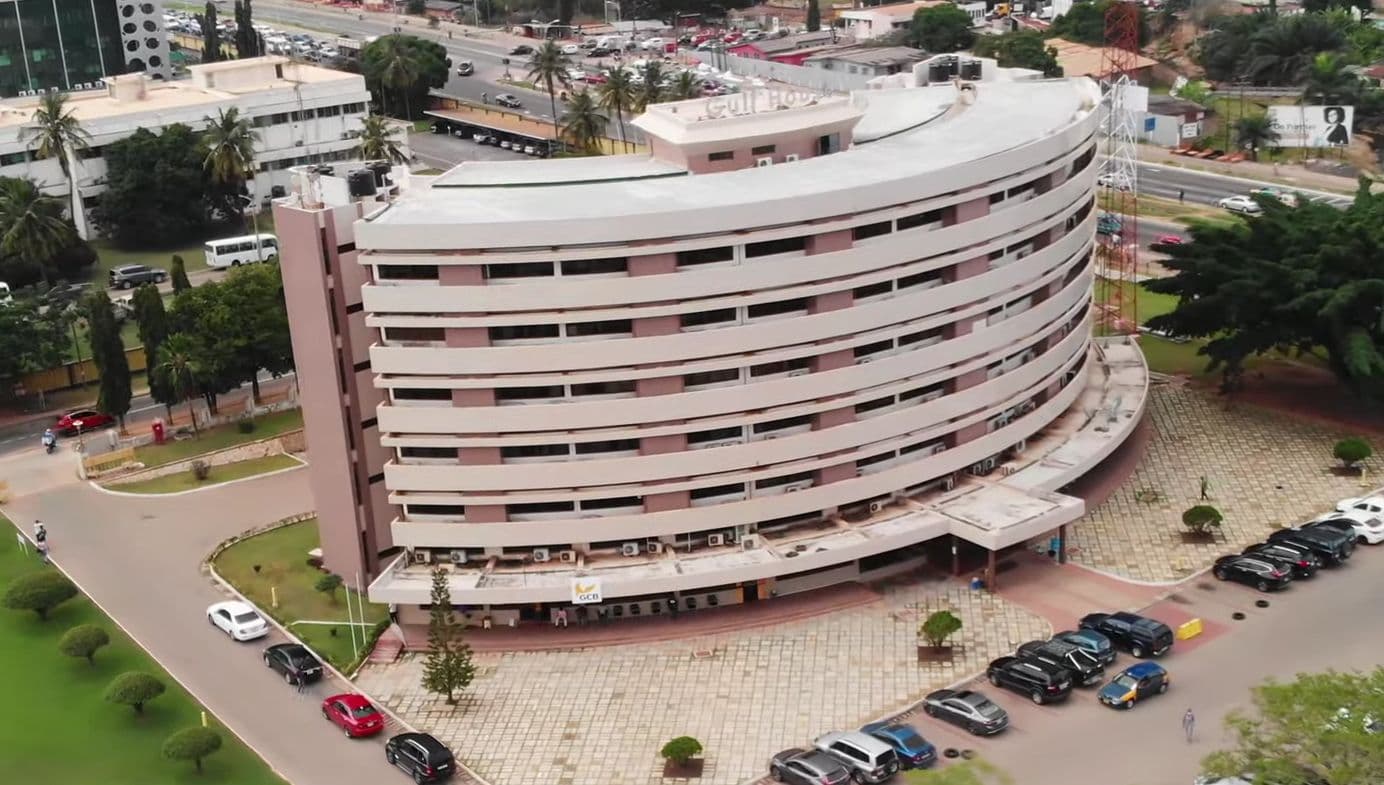 A large, modern, curved multi-story building with many windows and cars parked around it.
