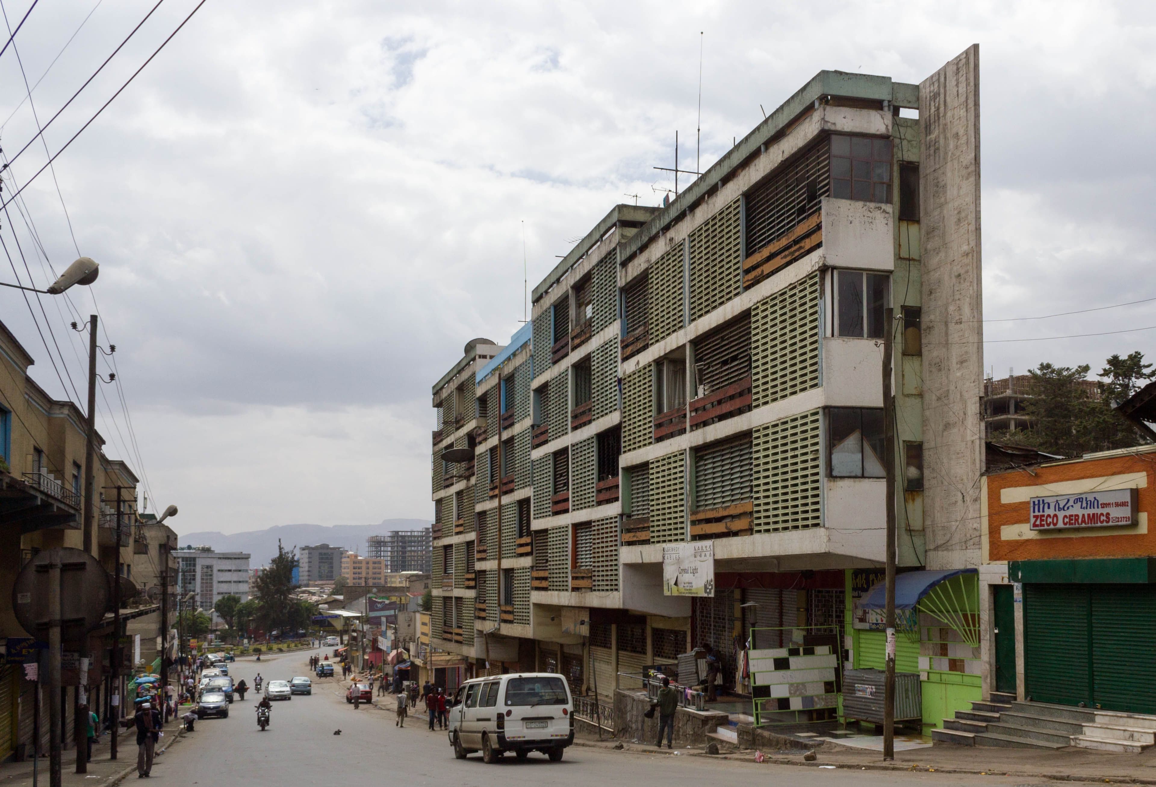 Modern apartment building with green balconies and angular design on a city street.
