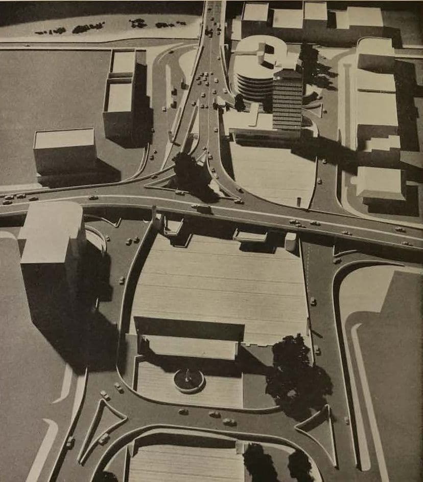 Grayscale architectural model of a complex urban interchange with roads, bridges, and buildings.