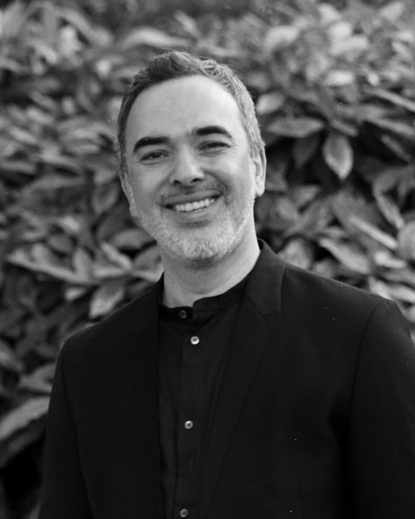 A black and white portrait of a smiling man with short, dark hair and a beard.
