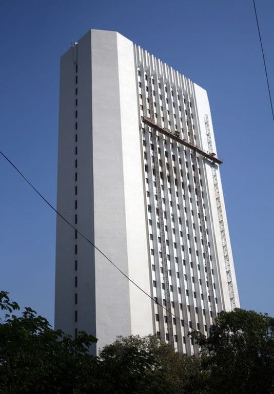 A tall, white, modern skyscraper with many windows against a bright blue sky.