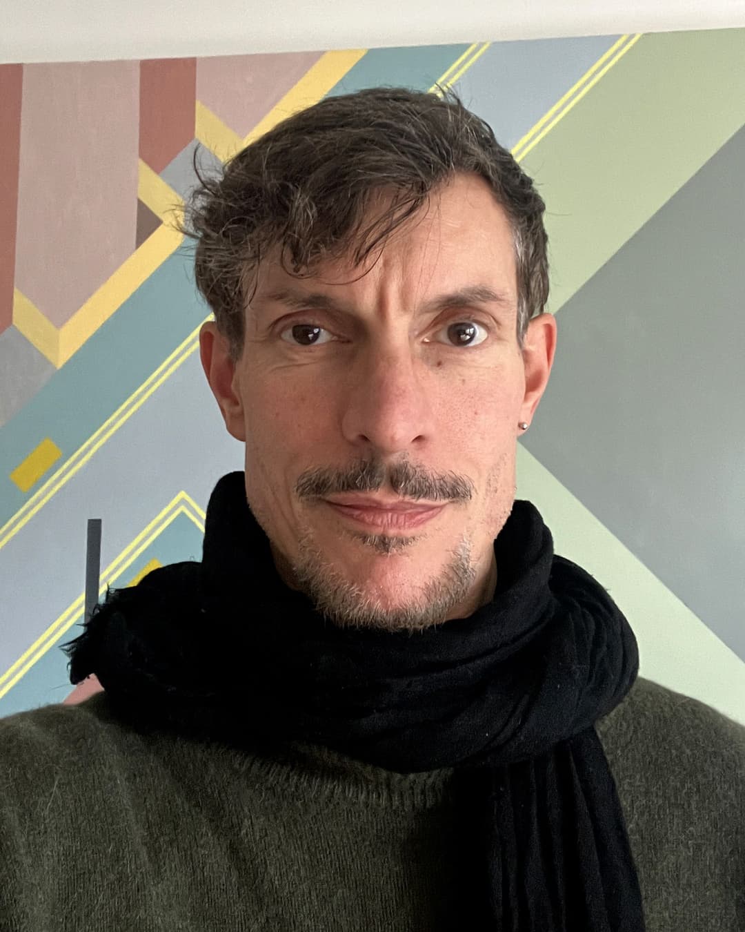 A man with a mustache and goatee wears a dark scarf and a green shirt.