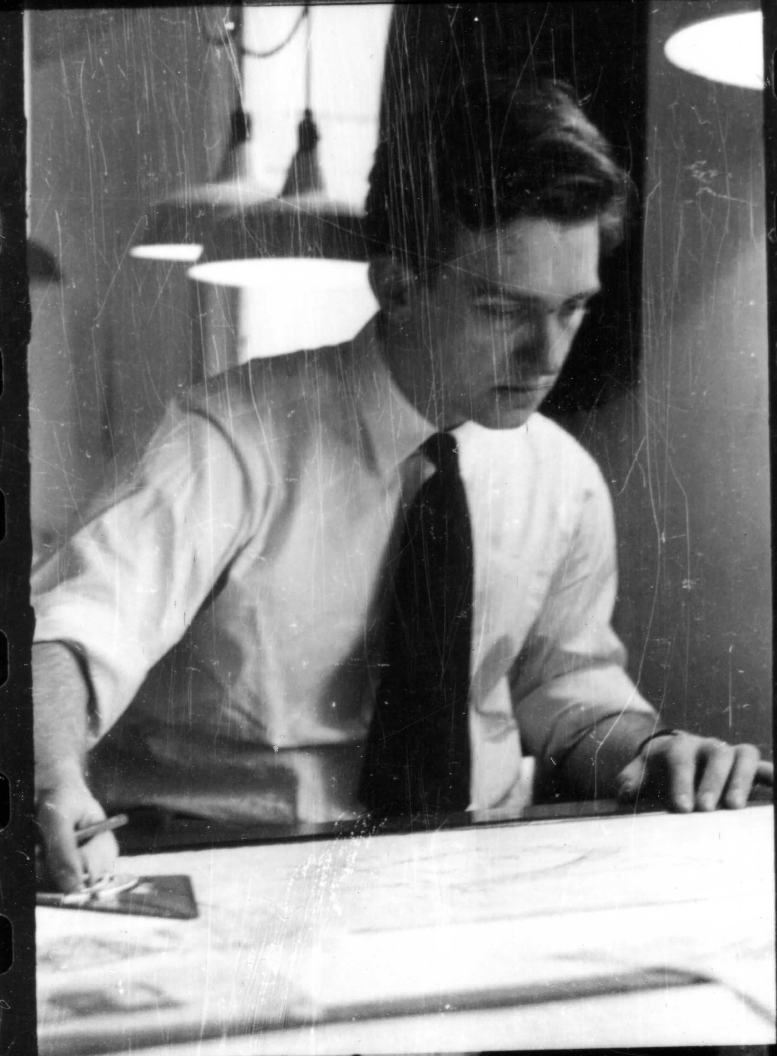 Man in shirt and tie using a T-square on a large sheet of paper.