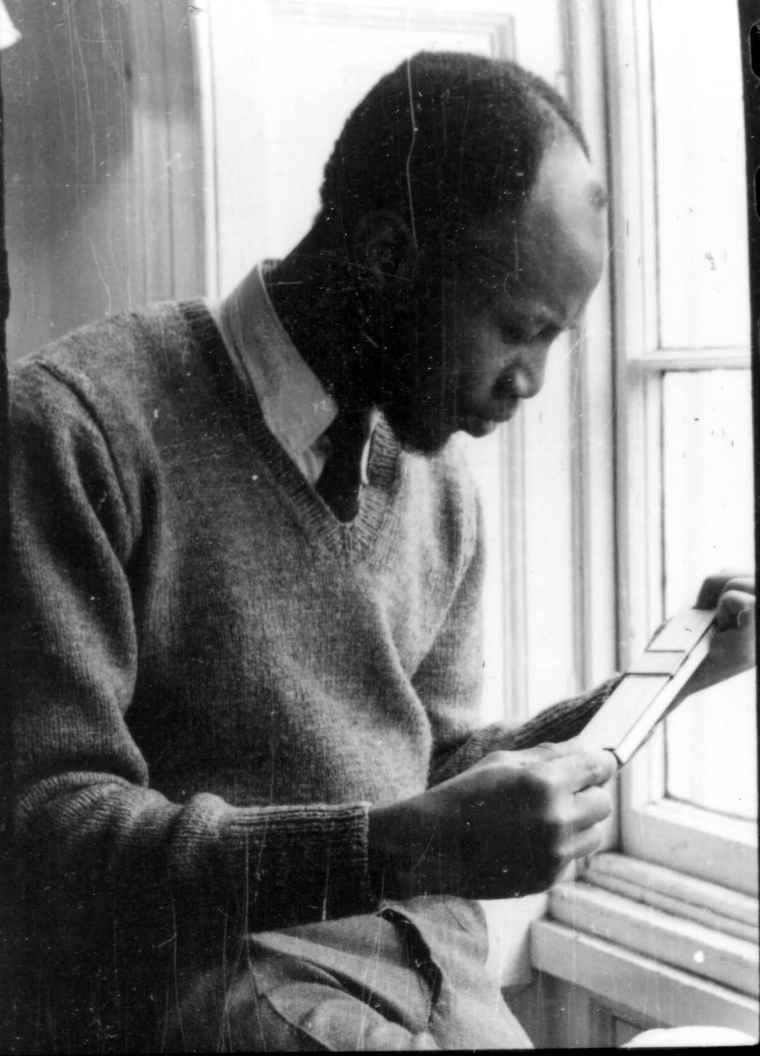Man in a sweater sitting by a window, examining small photos or cards.