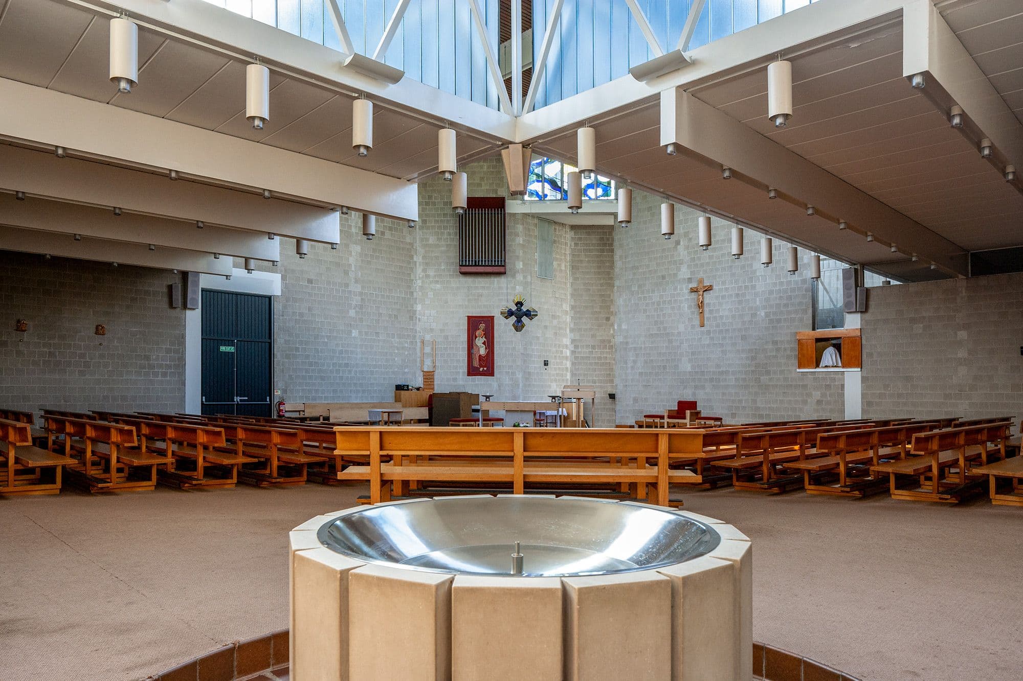 Modern church interior with a baptismal font, rows of wooden pews, and an altar.