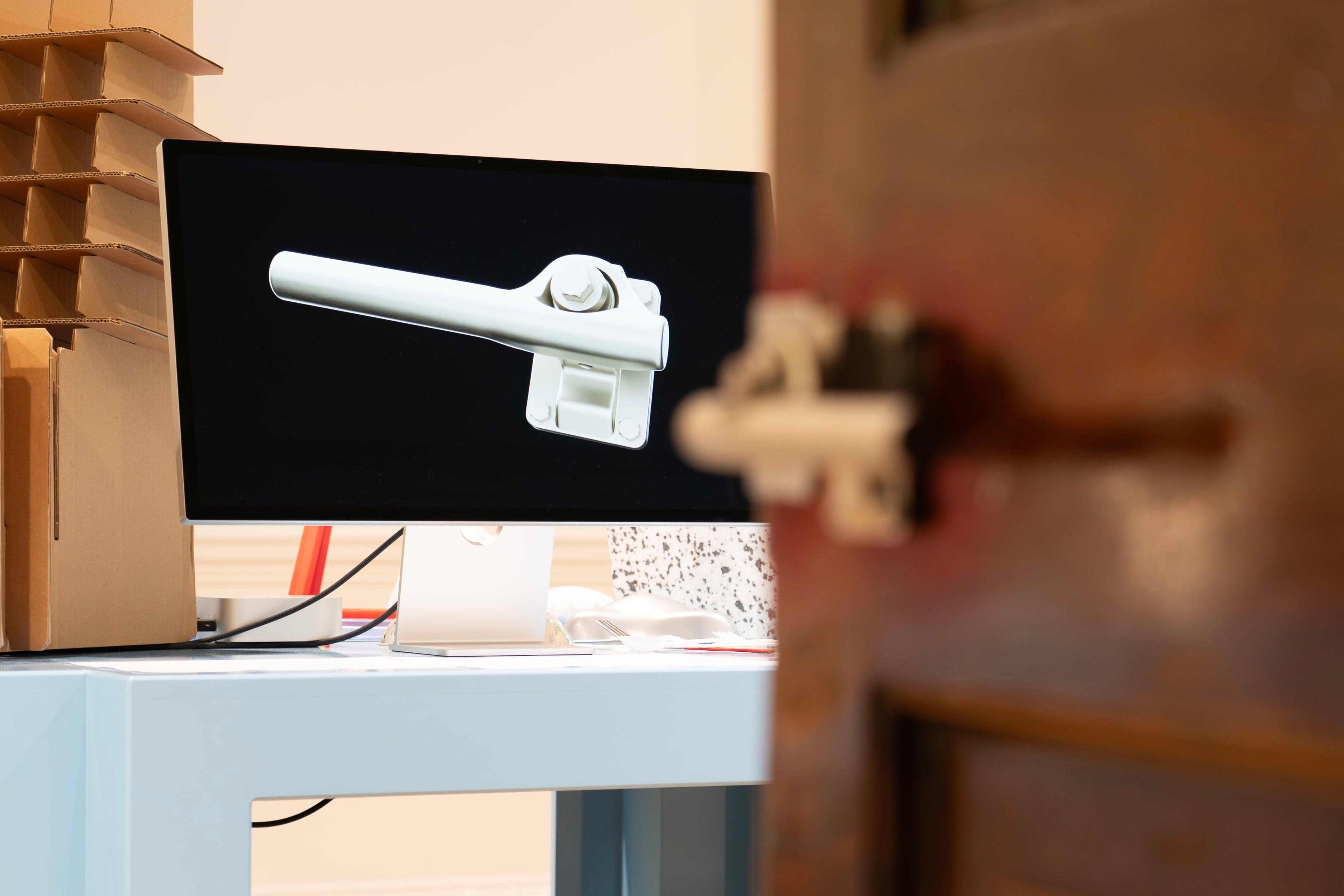 A door handle in the foreground, with a screen showing a render of the door handle design in the background.