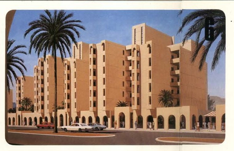 Modern desert-style building complex with arched windows and palm trees under a blue sky.