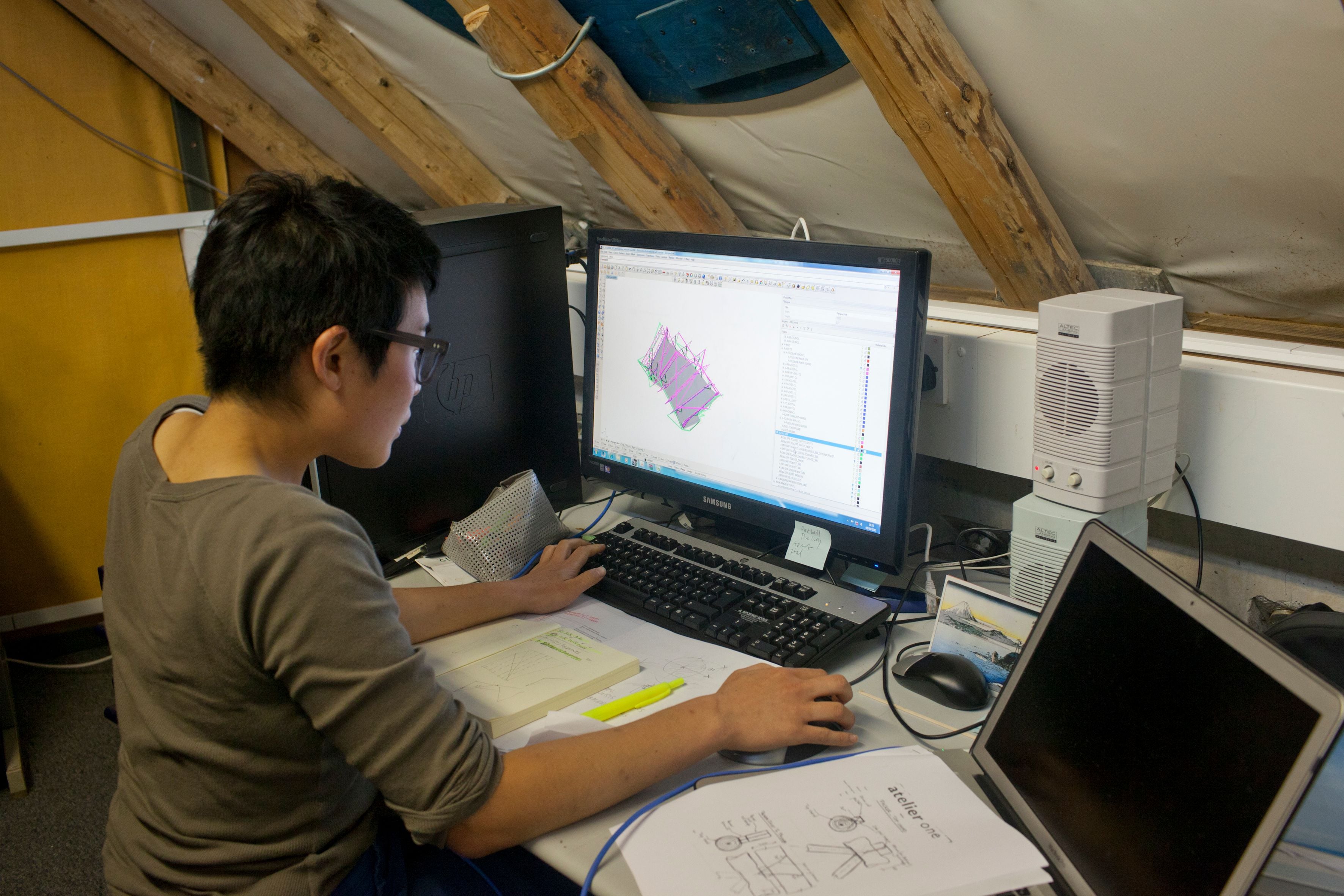 A student sits at a computer workstation creating a digital architectural model.