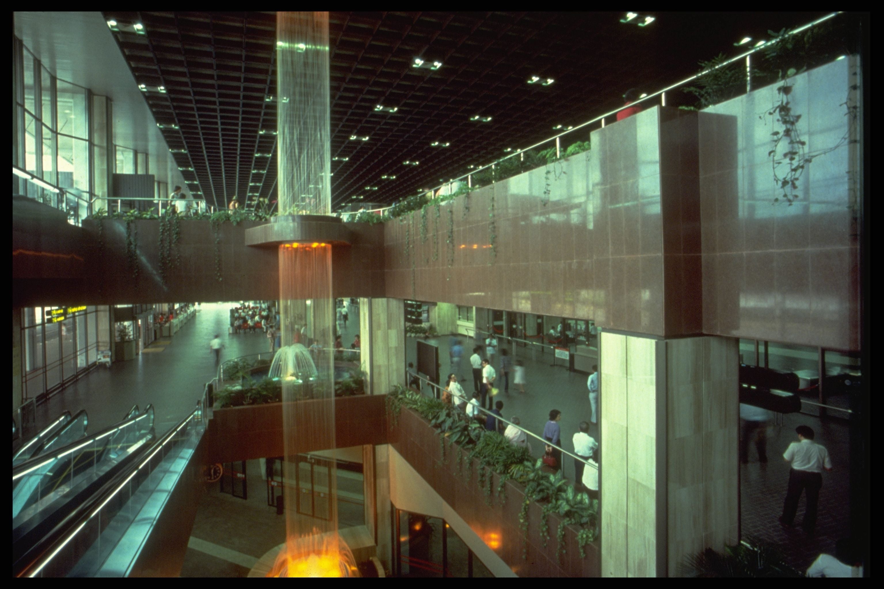 Modern, multi-level indoor building with a tall cylindrical water feature and people moving about.