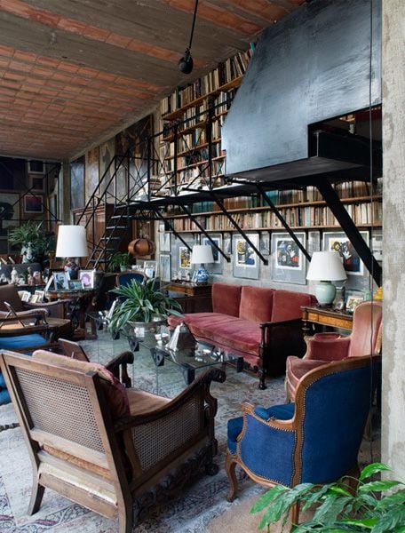 Eclectic living room with vintage sofa, blue and wood armchairs, bookshelves, and plants.