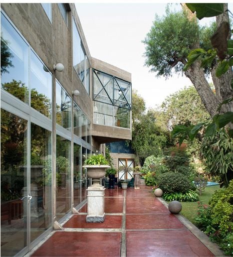 Modern building with large glass windows, a terracotta path, and a lush outdoor garden.