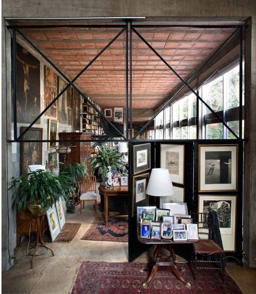 Long, narrow room with industrial black metal-framed windows, high ceiling, and eclectic decor.