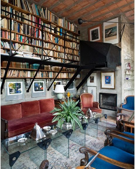 A cozy living room featuring a massive bookshelf, red sofa, and an unusually mounted television.