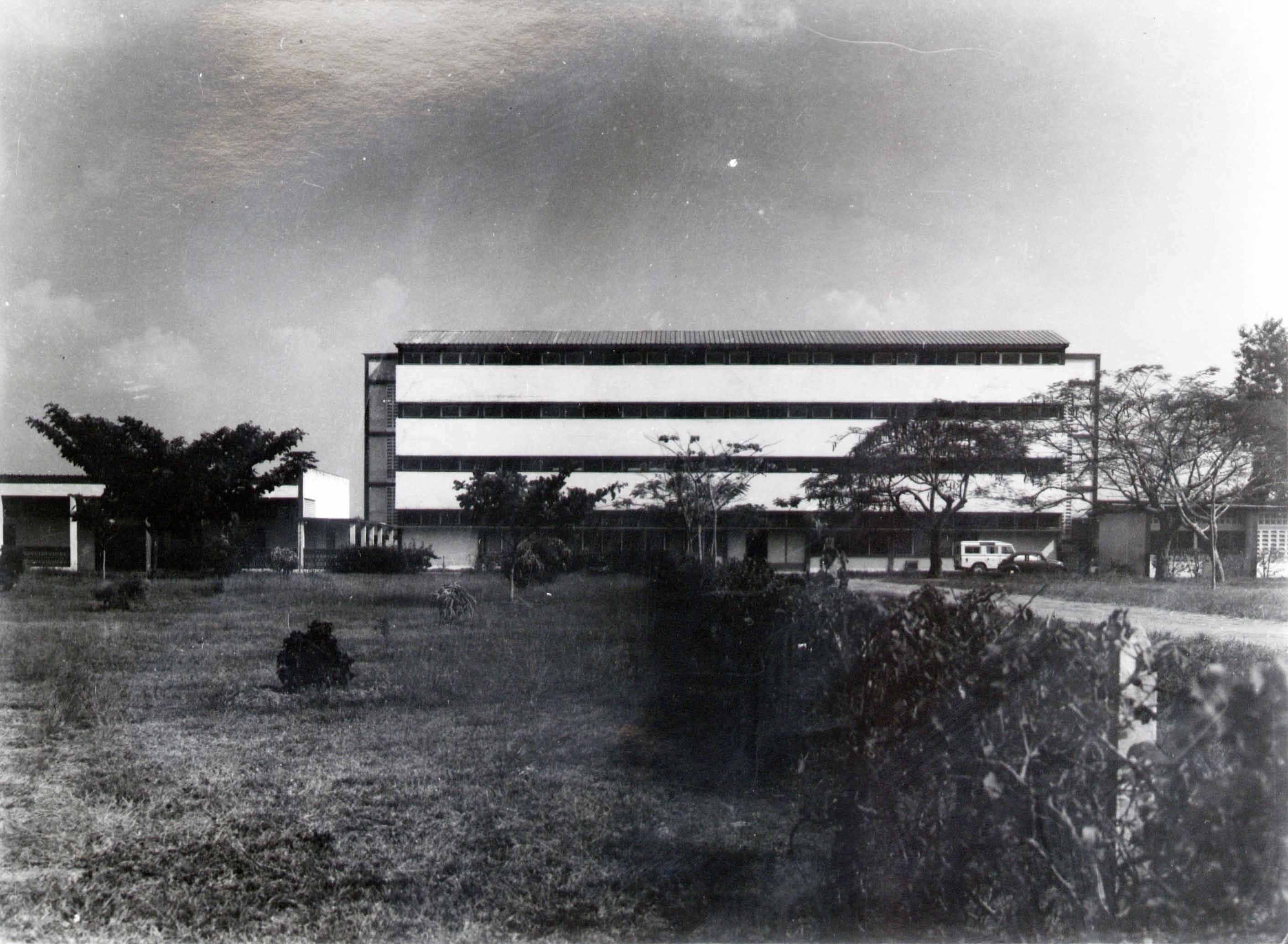 A large, modern, rectangular building with horizontal white bands under a cloudy sky.