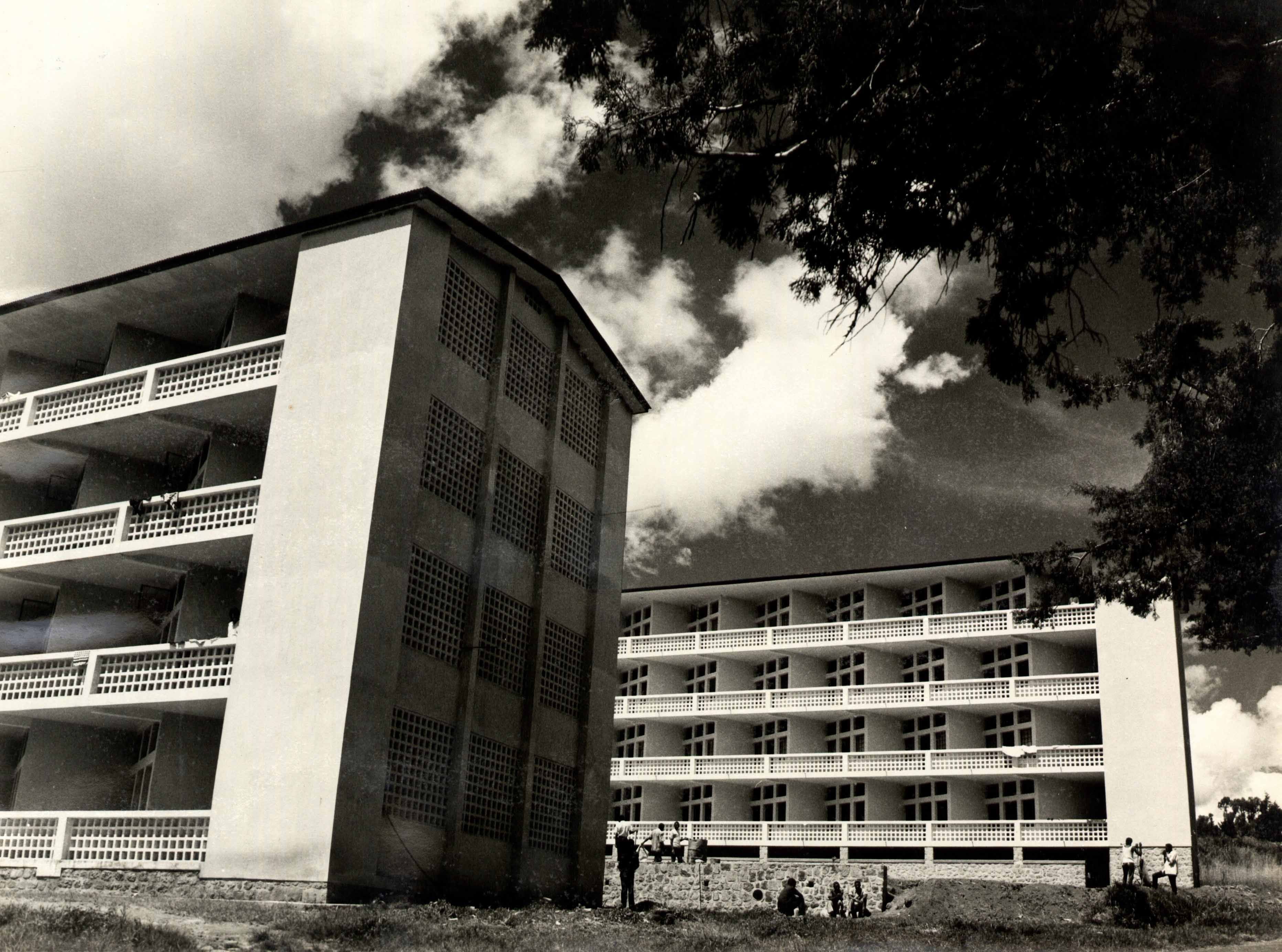 Two mid-century modernist apartment buildings with balconies stand under a dramatic cloudy sky.