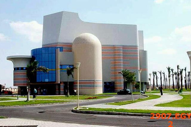 Modern cream and blue building with curved architecture surrounded by green grass and paved roads.