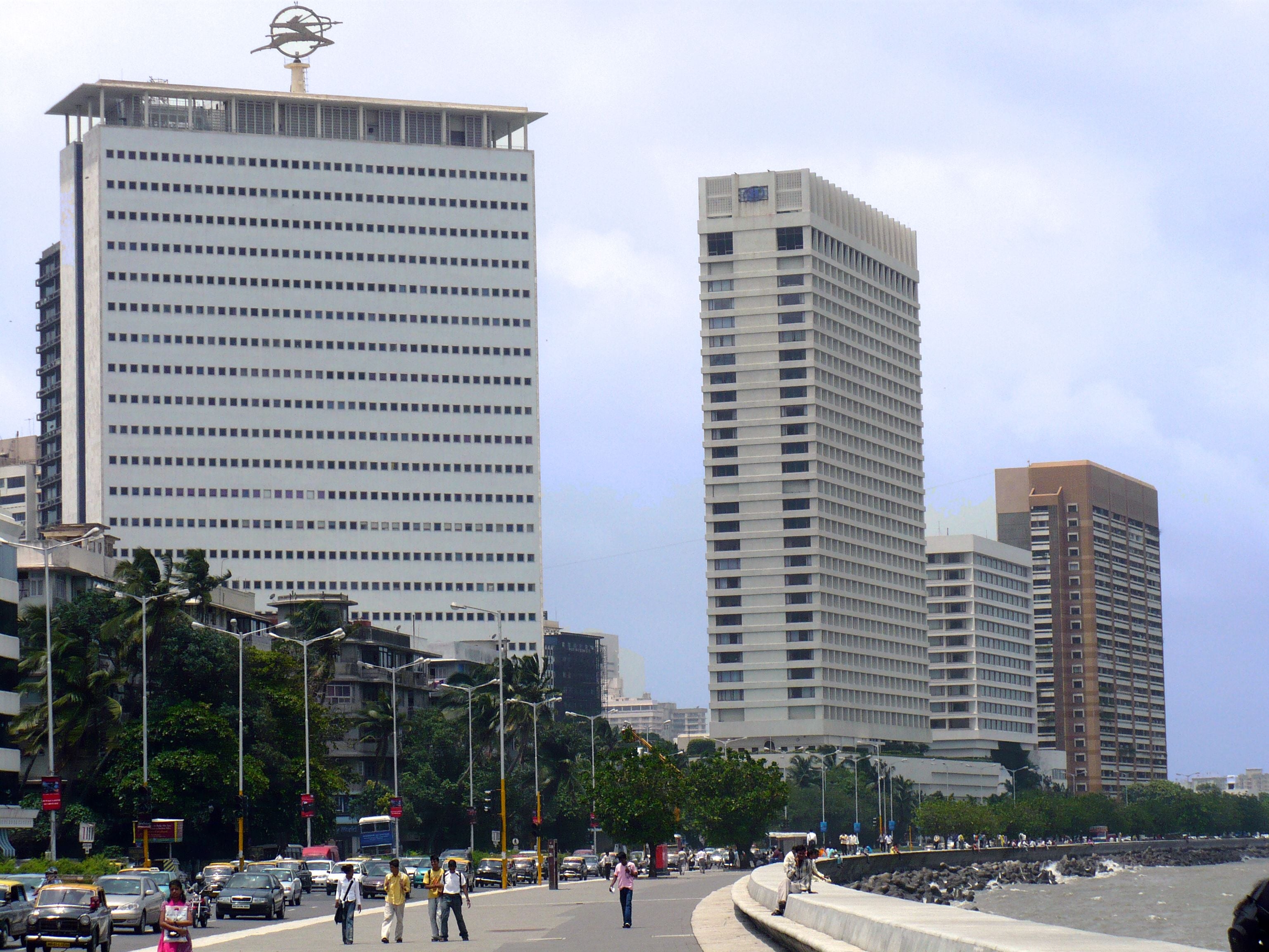 Modern white skyscrapers stand tall along a waterfront promenade with people walking and cars on the road.