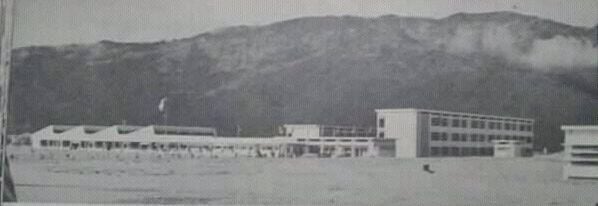 Black and white photo of campus buildings with a large, forested mountain behind them.