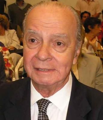 Headshot of an older man with a bald head, dark suit, and patterned tie.