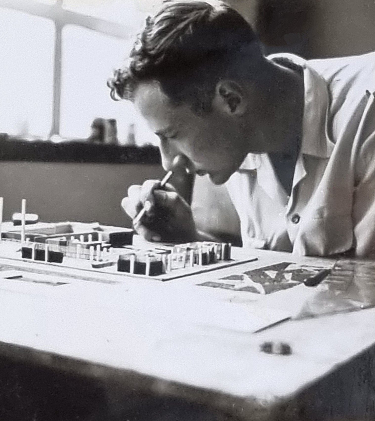 Man intently working on a detailed architectural model with small tools.