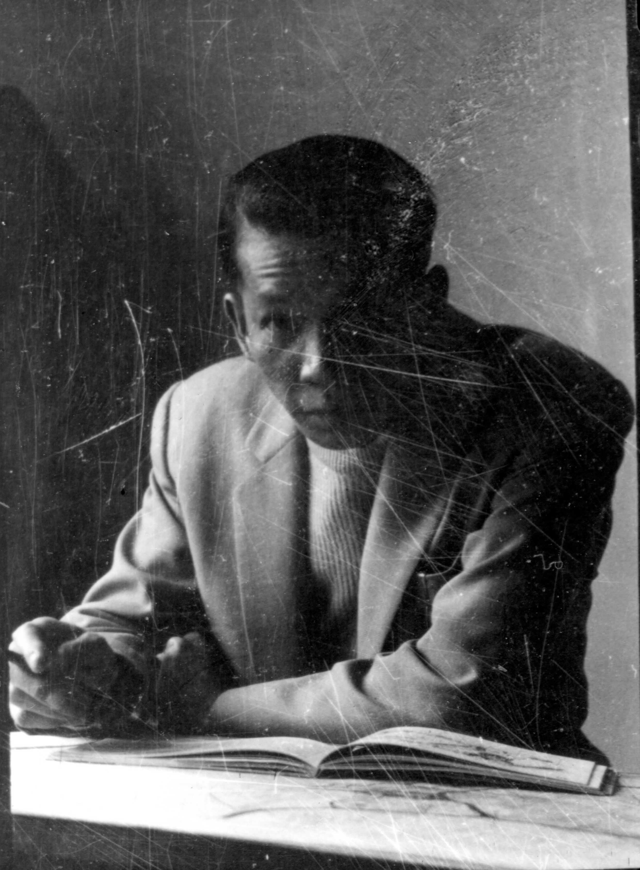 Man in a light suit jacket with arms crossed on a table with an open book.