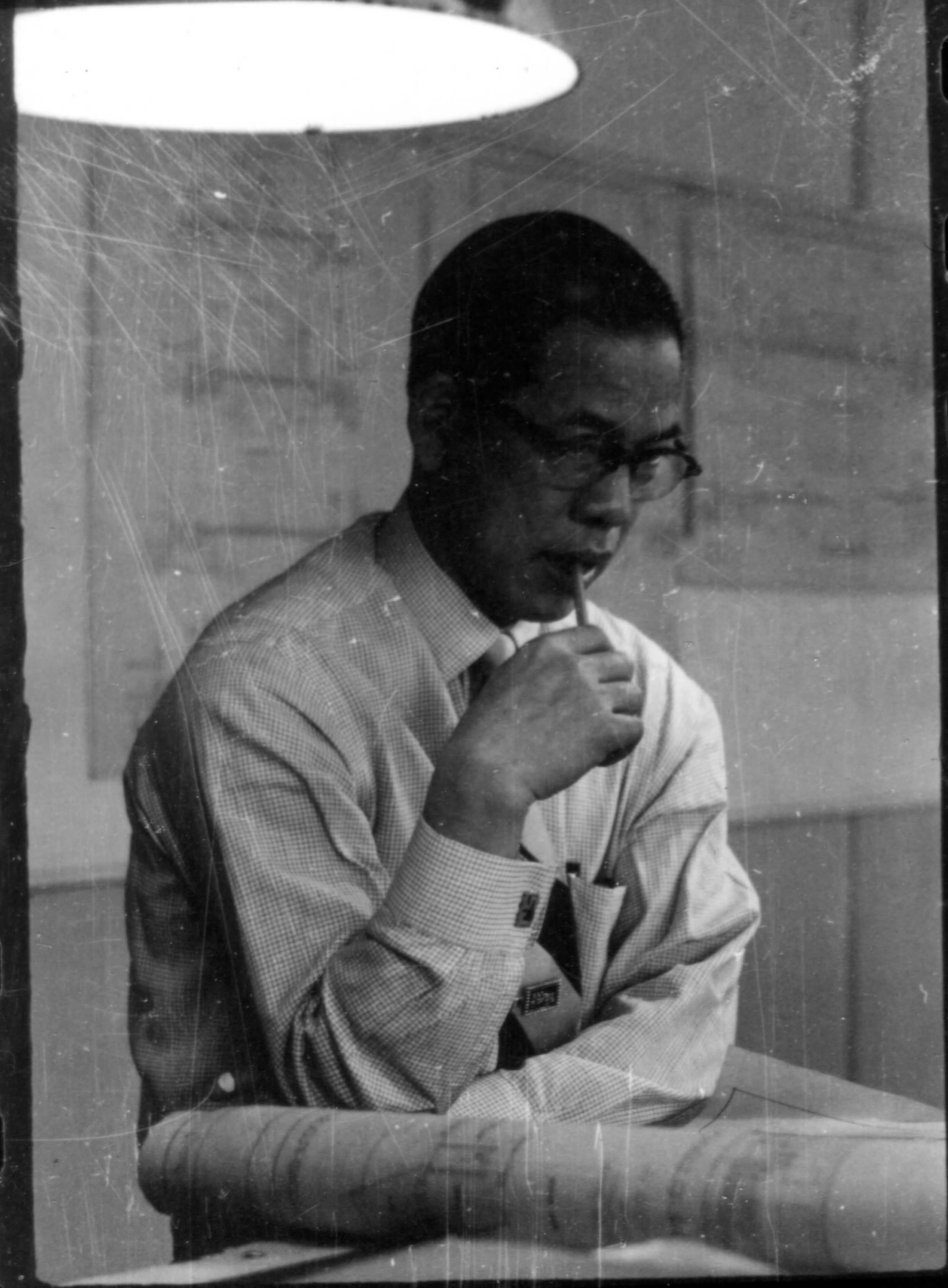 Man in glasses, shirt, and tie sitting at a desk, chin resting on his fist.