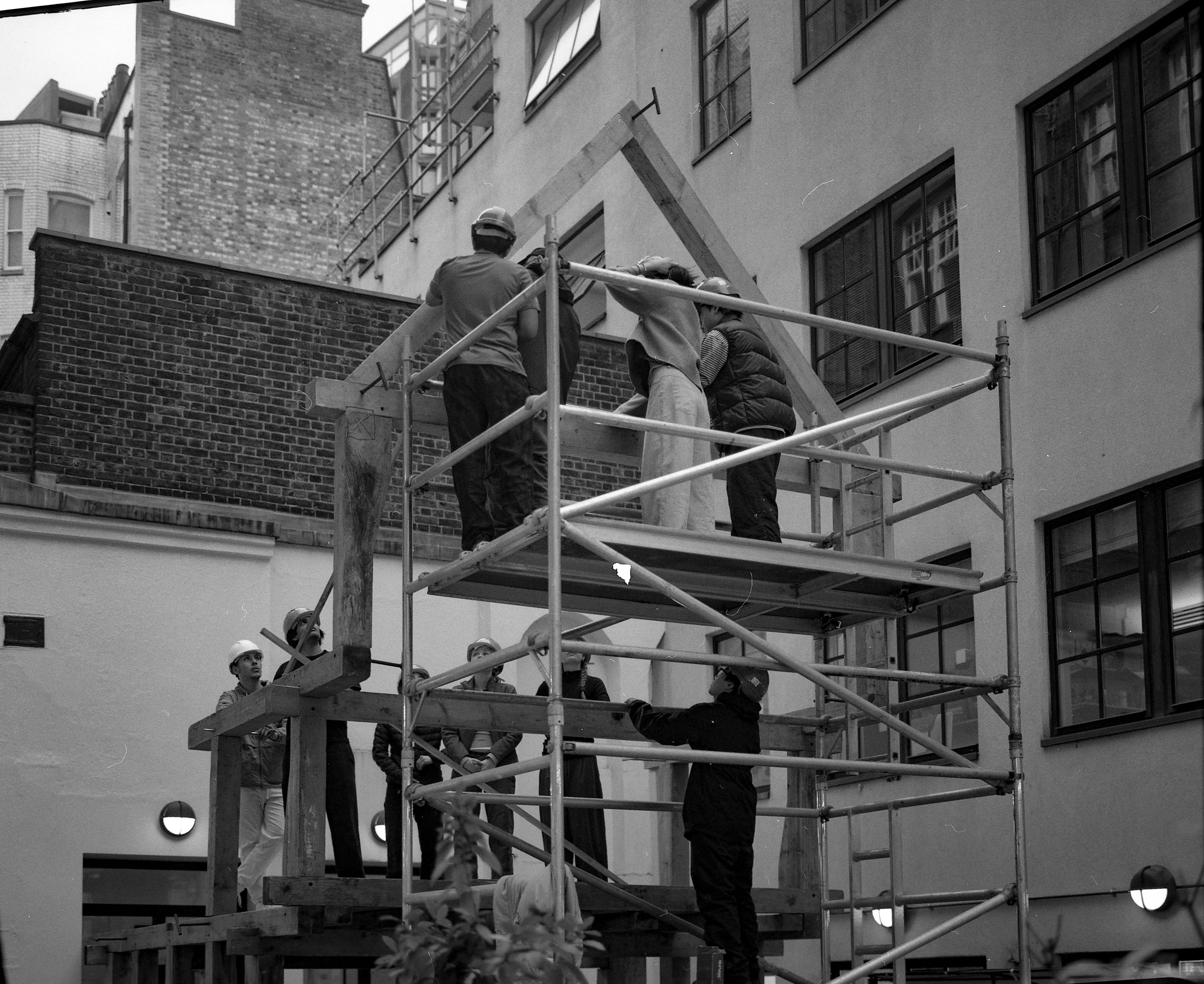 Black and white photograph of people on scaffolding building a wooden structure