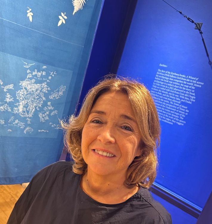 A woman with blonde shoulder-length hair smiles in front of a display with blue accents.